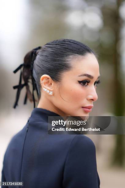 Heart Evangelista wears bejeweled / diamond earrings, lipstick, make-up , a ponytail, a turtleneck collar navy blue dress, outside Dior, during the...