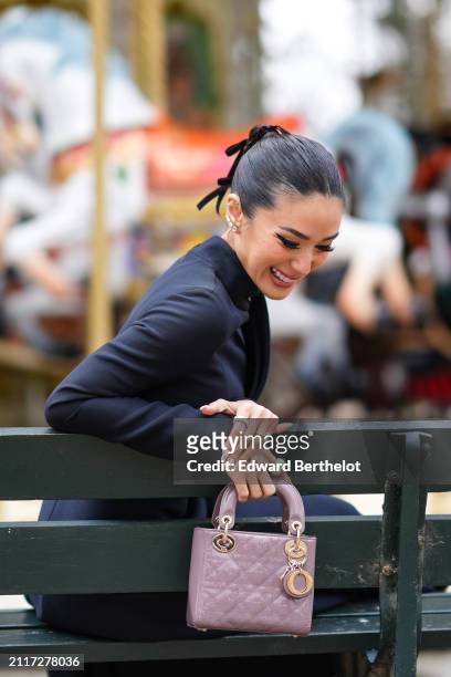 Heart Evangelista wears bejeweled earrings, make-up, lipstick, a navy blue turtleneck dress, a mauve / purple shiny quilted leather Lady Dior bag,...