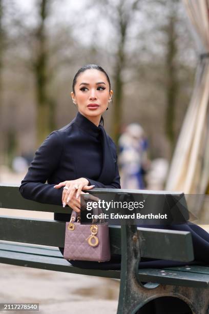 Heart Evangelista wears bejeweled earrings, make-up, lipstick, a navy blue turtleneck dress, a mauve / purple shiny quilted leather Lady Dior bag,...