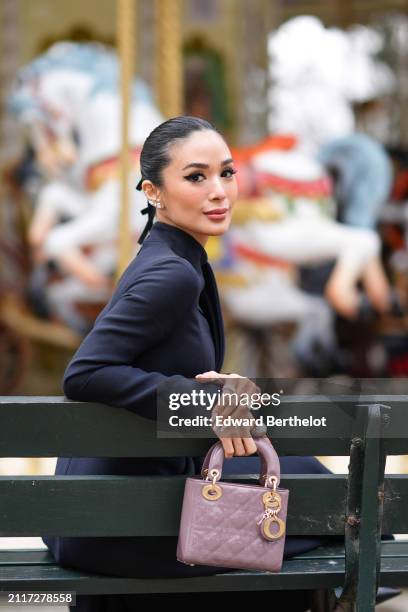 Heart Evangelista wears bejeweled earrings, make-up, lipstick, a navy blue turtleneck dress, a mauve / purple shiny quilted leather Lady Dior bag,...