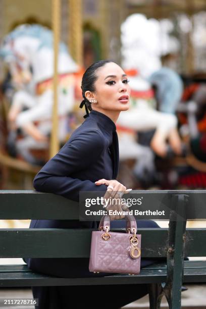 Heart Evangelista wears bejeweled earrings, make-up, lipstick, a navy blue turtleneck dress, a mauve / purple shiny quilted leather Lady Dior bag,...