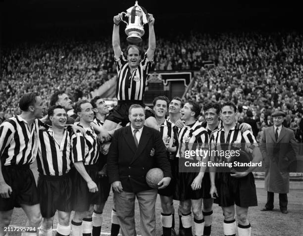 Newcastle United Football Club captain Jimmy Scoular holds up the FA Cup while carried on his teammates' shoulders and in front of manager Doug...