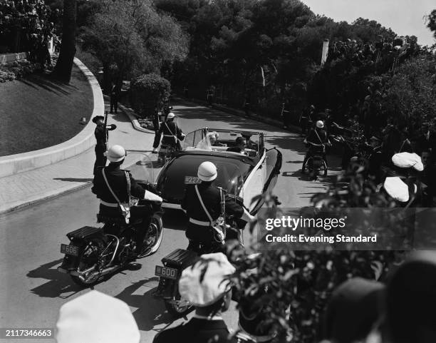 Grace Kelly and husband Prince Rainier III of Monaco drive away from Saint Nicholas Cathedral in a convertible car and a police escort following...