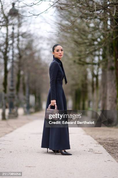 Heart Evangelista wears a dark navy blue turtleneck long maxi dress with shoulder pads, a mauve shiny quilted leather Lady Dior bag, black leather...