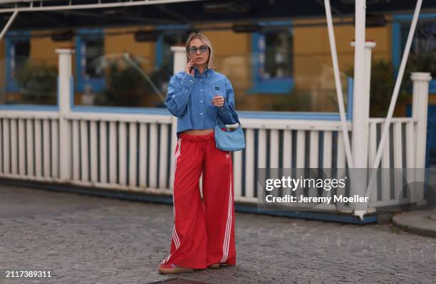 Karin Teigl seen wearing Rhude grey sunglasses, Miu Miu blue cotton cropped buttoned shirt, Adidas red long wide leg track pants, Prada Re-edition...