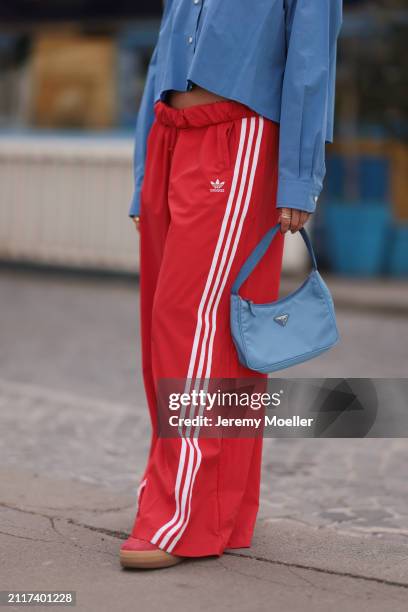 Karin Teigl seen wearing Miu Miu blue cotton cropped buttoned shirt, Adidas red long wide leg track pants, Prada Re-edition blue nylon bag, Bulgari...