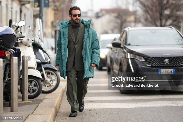 Guest wears sunglasses, a green oversized winter jacket , a wool turtleneck pullover , a green khaki oversized blazer jacket , suit pants , black...