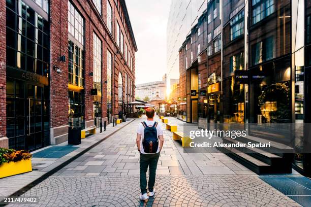 rear view of a man with backpack walking in the streets of aker brygge district, oslo, norway - oslo business stock pictures, royalty-free photos & images