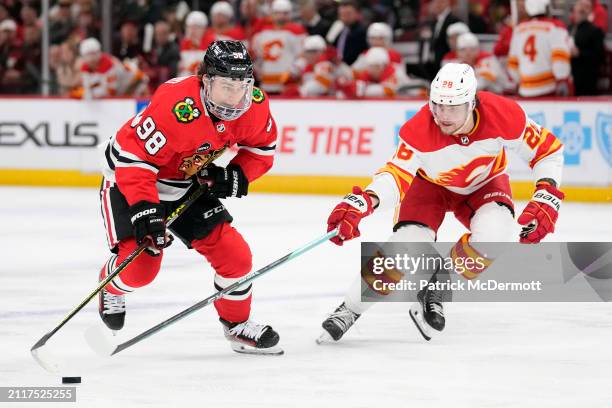 Connor Bedard of the Chicago Blackhawks skates with the puck against Nikita Okhotiuk of the Calgary Flames during the second period at the United...