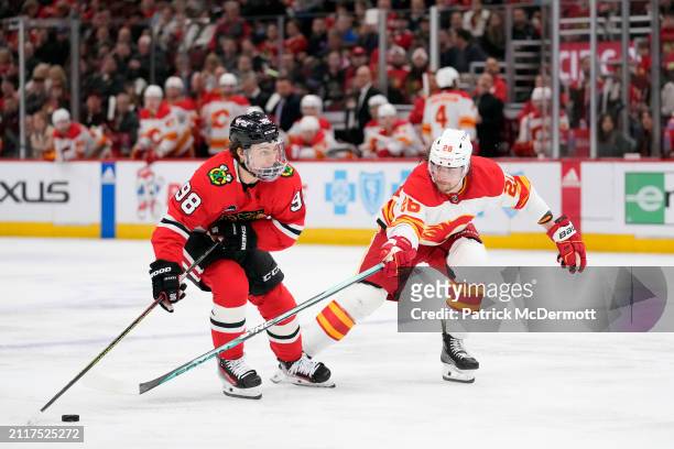 Connor Bedard of the Chicago Blackhawks skates with the puck against Nikita Okhotiuk of the Calgary Flames during the second period at the United...