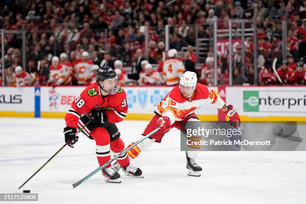 Connor Bedard of the Chicago Blackhawks skates with the puck against Nikita Okhotiuk of the Calgary Flames during the second period at the United...