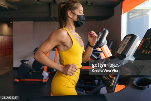 mid waist portrait of blonde woman running in the treadmill with protective face mask indoors - vita shorts fotografías e imágenes de stock