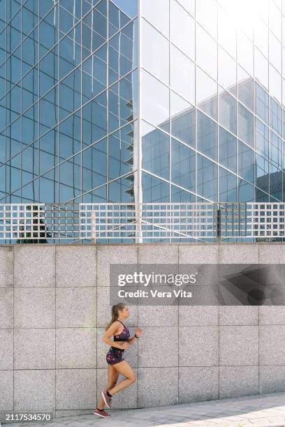 full length view of blonde woman running in the street with financial buiding in the background - vita shorts fotografías e imágenes de stock