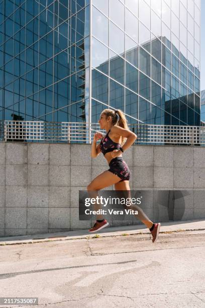 full length view of blonde woman running in the street with financial buiding in the background - vita shorts fotografías e imágenes de stock