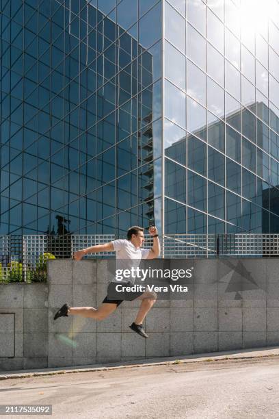 full length view of young man running in the street with financial buiding in the background - vita shorts fotografías e imágenes de stock