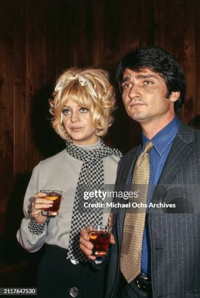 American actress Goldie Hawn, wearing a grey top with grey-and-black checked cuffs and a grey-and-black checked scarf, with her husband, American...