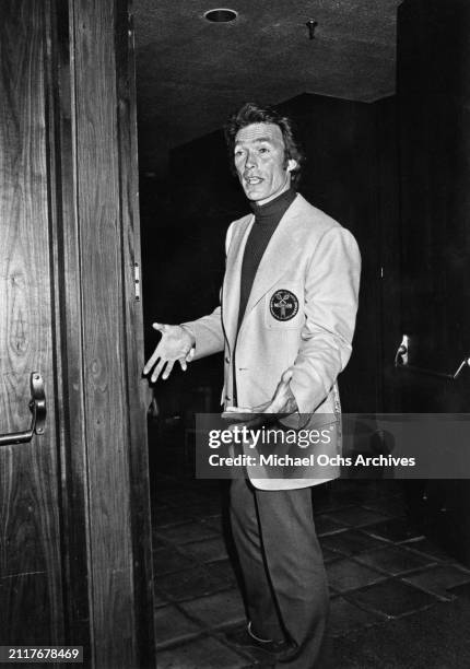 American actor and film director Clint Eastwood, wearing a light blazer over a dark turtleneck sweater, stands with his palms turned up, in an open...