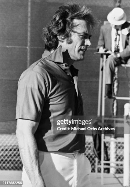 American actor and film director Clint Eastwood, wearing a dark polo shirt and white shorts, while playing tennis, United States, circa 1975.