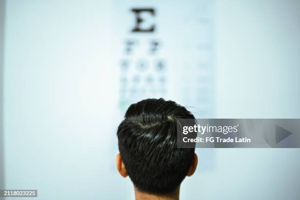 child boy doing exam looking the eye chart at optics - astigmatismo imagens e fotografias de stock