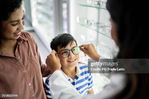 mother and son buying a glasses and talking with optician at optical store - eyeglasses stock pictures, royalty-free photos & images
