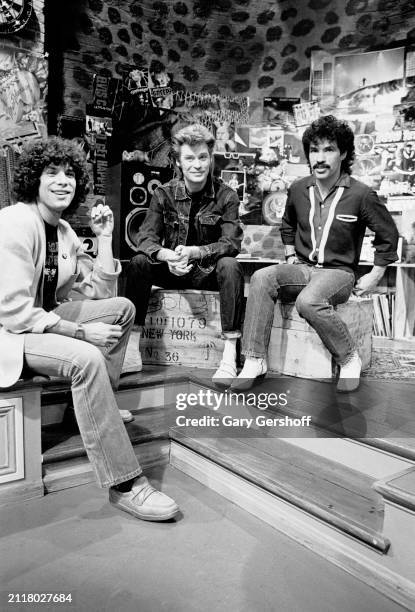 View of, from left, MTV VJ Mark Goodman and American Pop musicians Daryl Hall & John Oates, both of the duo Hall & Oates, as they all sit on a low...