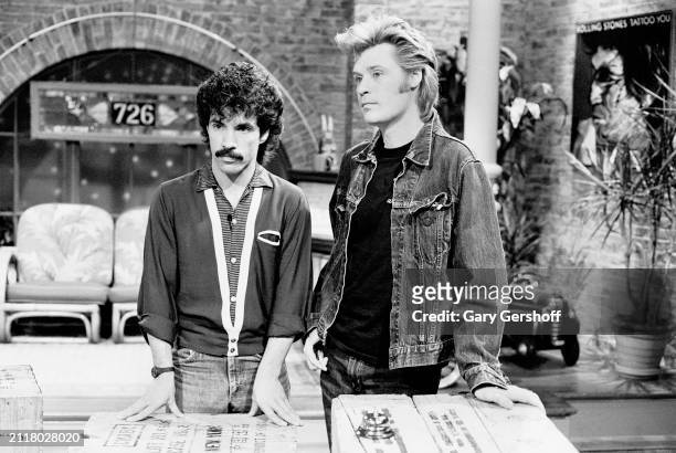 View of American Pop musicians John Oates and Daryl Hall as they stand behind several crates during an interview on MTV at Teletronic Studios, New...