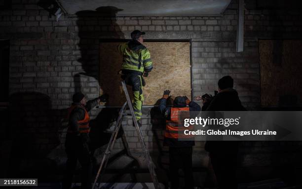 Municipal service workers close windows of a residential building in the Shevchenkivskyi district, broken by a Russian aerial bombardment, with OSB...