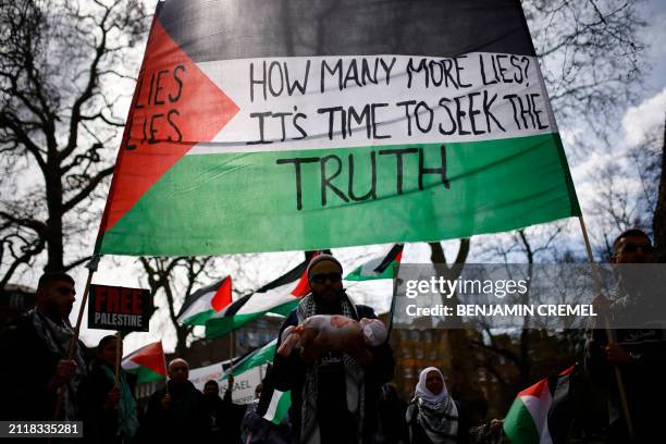 Protester holds a doll wrapped in a red paint-stained shroud as Pro-Palestinian activists and supporters wave flags and hold placards during a...