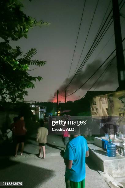 People watch a fire in the distance from a street in Bogor, West Java, on March 30, 2024. Multiple explosions ripped through a military ammunition...