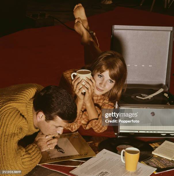 Young couple lie on the floor of a room to listen to long playing records on a portable record player, England, 19th January 1963. The woman holds a...