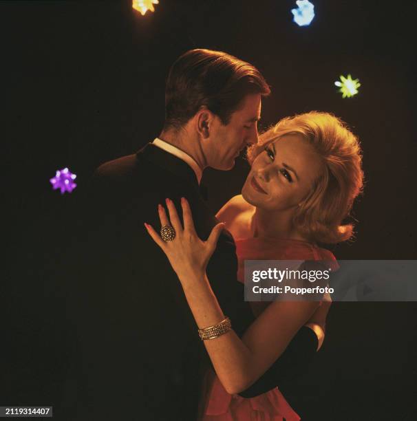 Posed studio portrait of a couple embracing as they dance to music, the man wears a suit and the woman wears a red evening gown, London, 19th January...