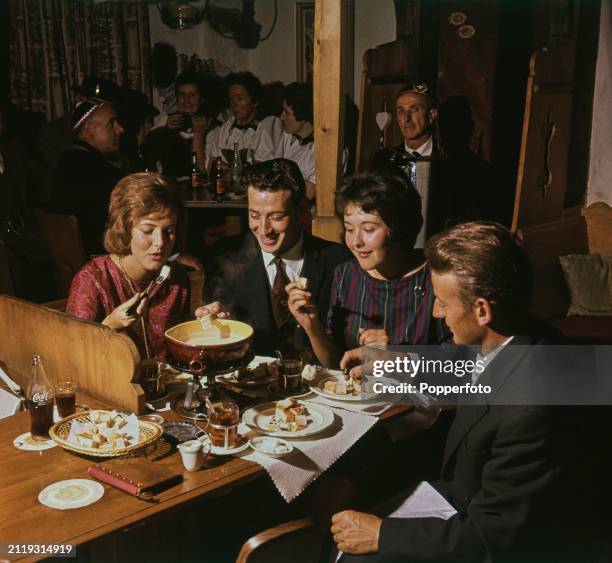 Guests enjoy a fondue dish of melted cheese and wine served in a heated pot with cubes of bread on their table at a restaurant during a holiday in...