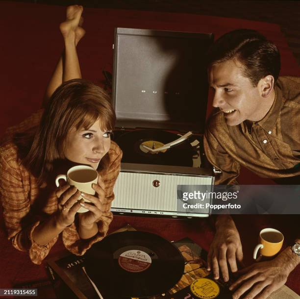 Young couple lie on the floor of a room to listen to long playing records on a portable record player, England, 19th January 1963. The man looks...