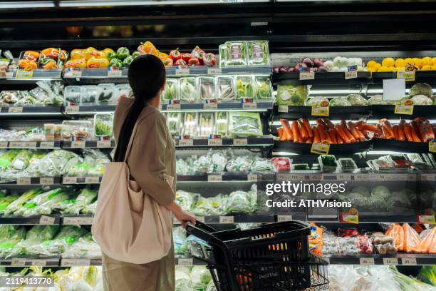 um comprador contemplativo examina a variedade de vegetais em uma mercearia, refletindo uma escolha consciente por um estilo de vida saudável. - passagem objeto manufaturado - fotografias e filmes do acervo