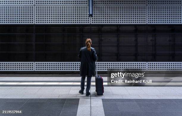 rearview of woman with luggage standing alone at railroad station platform - reinhard krull stock pictures, royalty-free photos & images