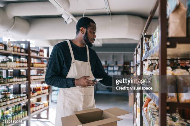 un trabajador africano de una tienda orgánica elige de manera experta los artículos para el pedido en línea de un cliente - dependiente de tienda fotografías e imágenes de stock