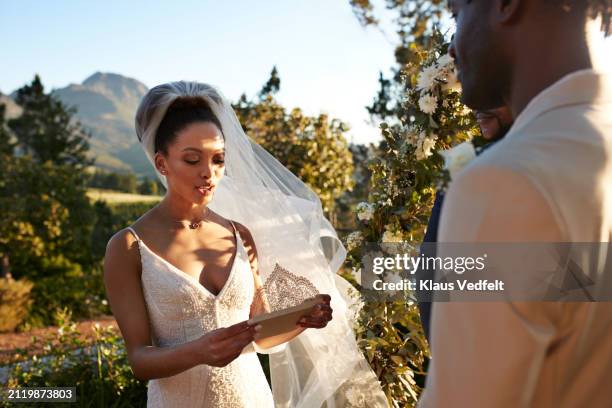 bride reading wedding vows in front of groom - promesas de matrimonio fotografías e imágenes de stock