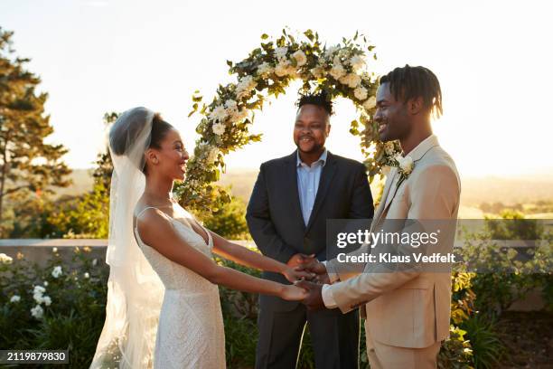 happy young couple holding hands standing by minister - promesas de matrimonio fotografías e imágenes de stock