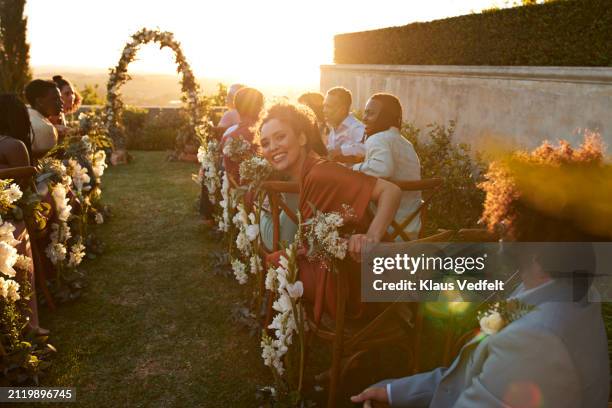 happy woman looking back while sitting amidst guests - gast stockfoto's en -beelden