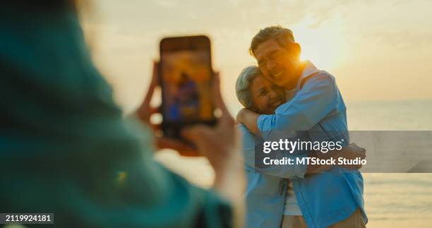 closeup of asian senior adult couple is photographed by a local female guide while traveling on vacation on beach enjoy sea at sunset light. happy elderly people lifestyle after retirement. - mes stock pictures, royalty-free photos & images