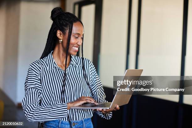 laughing young businesswoman standing in an office and working on a laptop - entrepreneur stockfoto's en -beelden