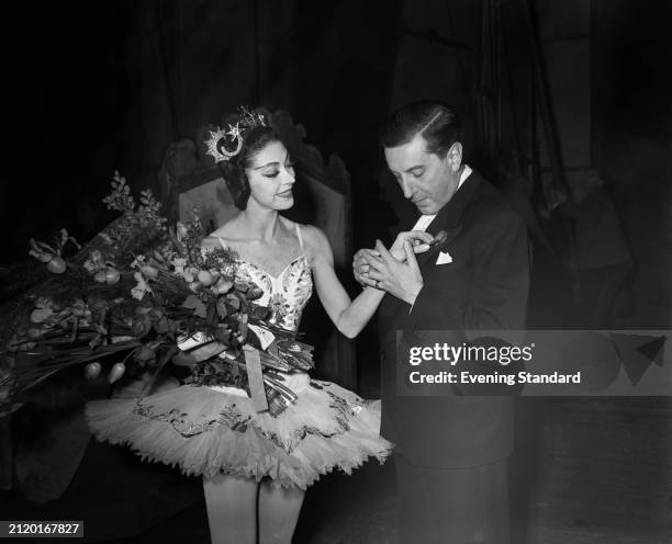 Dame Margot Fonteyn in stage costume holds a bouquet of flowers while choreographer Frederick Ashton clasps her hand backstage at a Gala ballet...