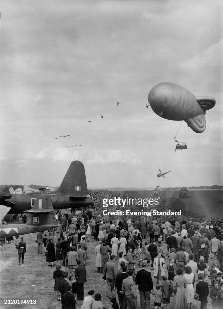 Barrage balloon floats above spectators at the Farnborough Air Show, Hampshire, September 9th 1955. A helicopter and jet fighters can be seen in the...