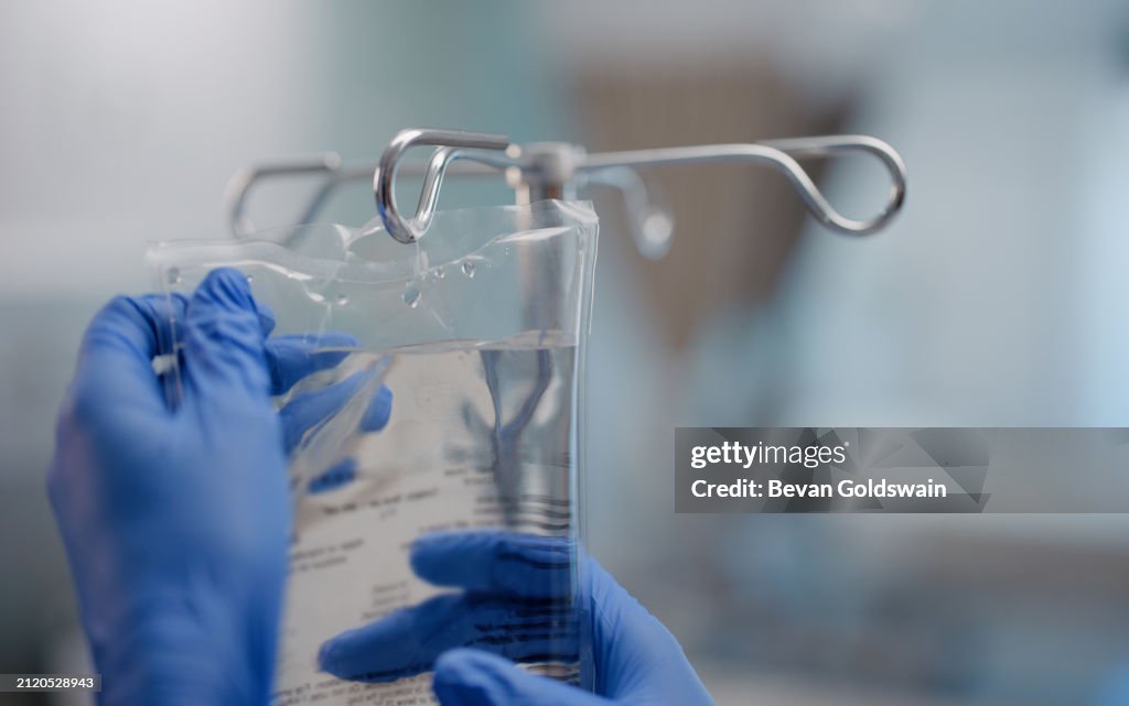 Hands, IV drip and saline solution in hospital, clinic and healthcare facility for health and healing. Doctor, nurse and closeup of medical equipment for intensive care, life support and medicine