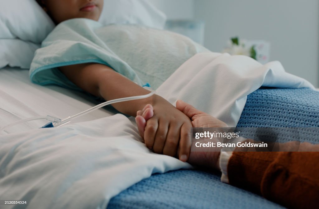 Hospital, holding hands and kid in bed with love, support and care in clinic after surgery. Child, healthcare and cancer patient with empathy, kindness and caregiver with compassion with help