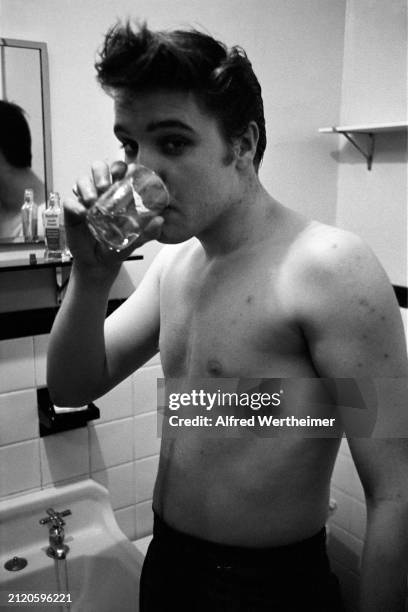 Alfred Wertheimer/MUUS Collection via Getty Images) American musician Elvis Presley drinks a glass of water in the bathroom of his suite at the...