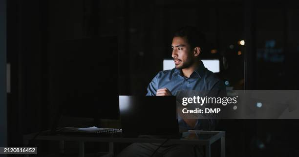 young man, thinking and computer at night for information technology, programming or cybersecurity solution. professional programmer or expert with problem solving or ideas on laptop in dark office - darkness stock pictures, royalty-free photos & images
