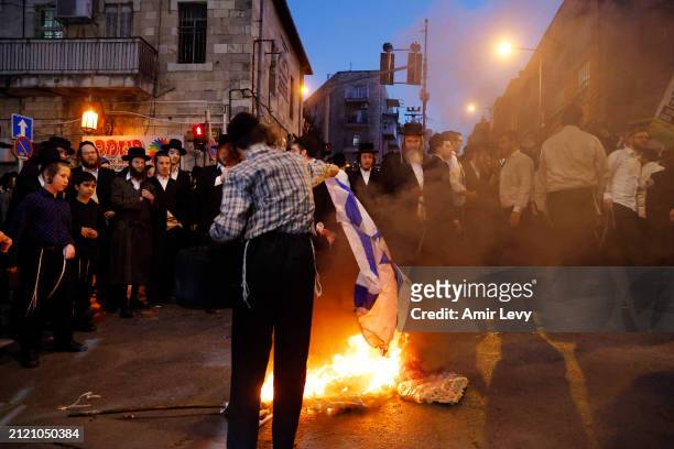 An ultra-orthodox jew burns an Israeli flag as anti-government protests are stepped up on March 31, 2024 in Meah Shearim, Jerusalem. Israelis...