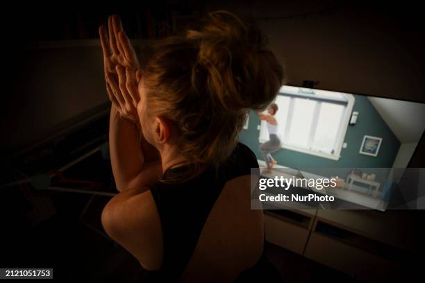 Woman is seen doing yoga exercises with YouTube trainer on a television in her living room in Warsaw, Poland on 23 March, 2024.