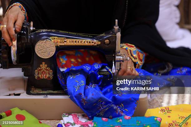 An Emirati woman sews during an annual heritage festival in Al-Ain on November 10, 2023. The art of hand-weaving braided shiny ribbons to adorn...